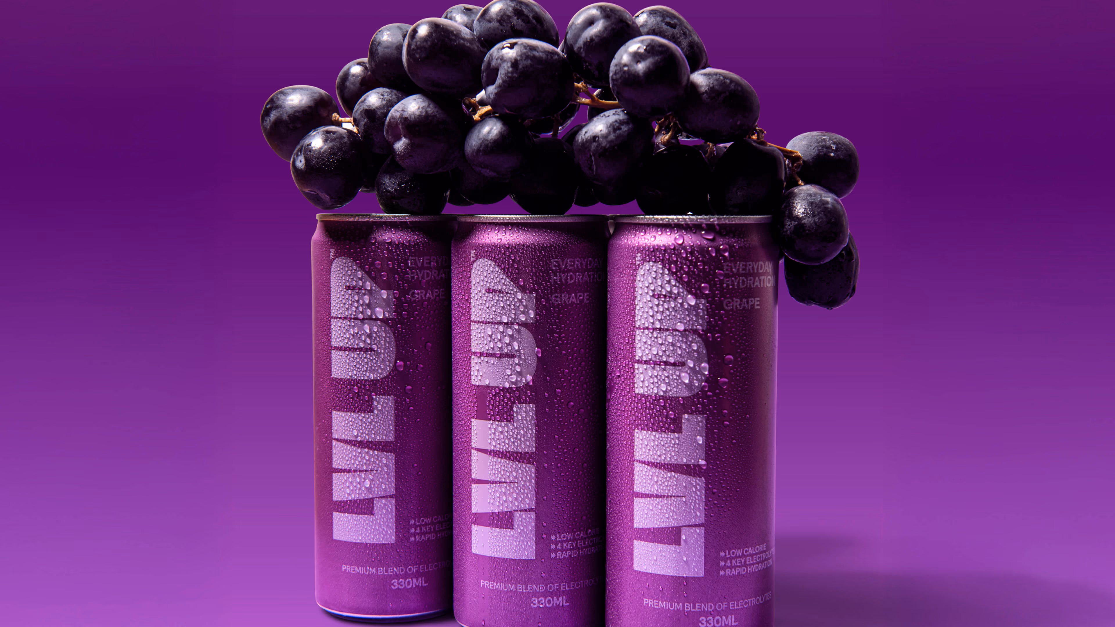 Three purple cans of LVL UP grape-flavored electrolyte drink with fresh grapes on top against a purple background.