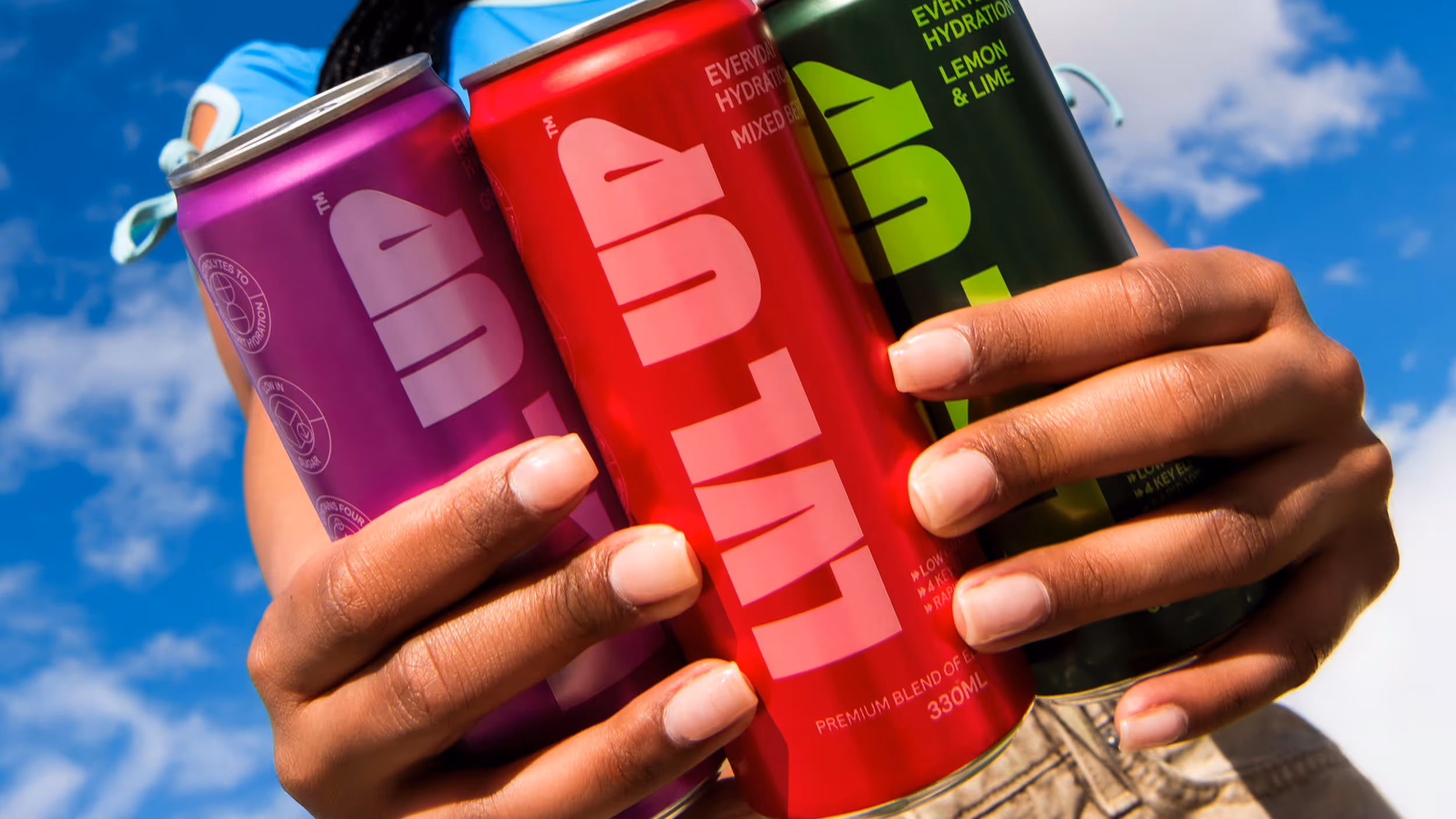 Person holding three colorful cans of LVLUP hydration drink against a blue sky background.