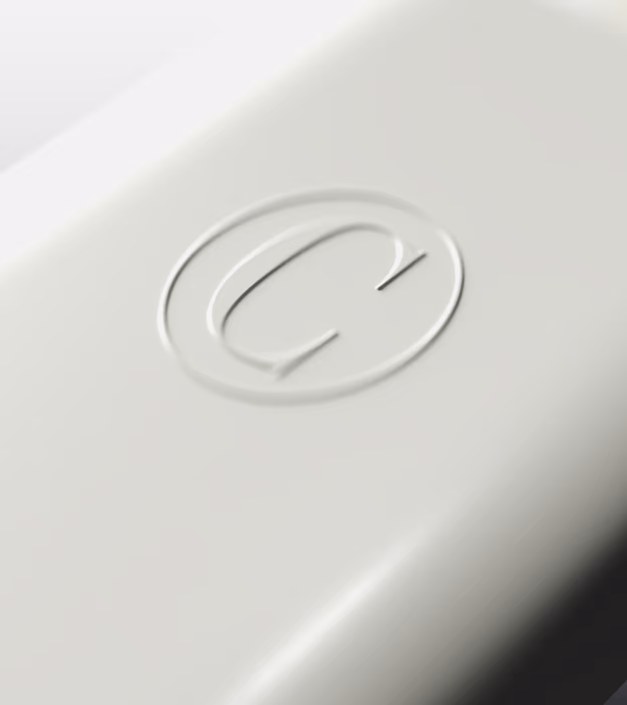Close-up of a smooth light gray surface with an embossed circular logo featuring a stylized letter G.