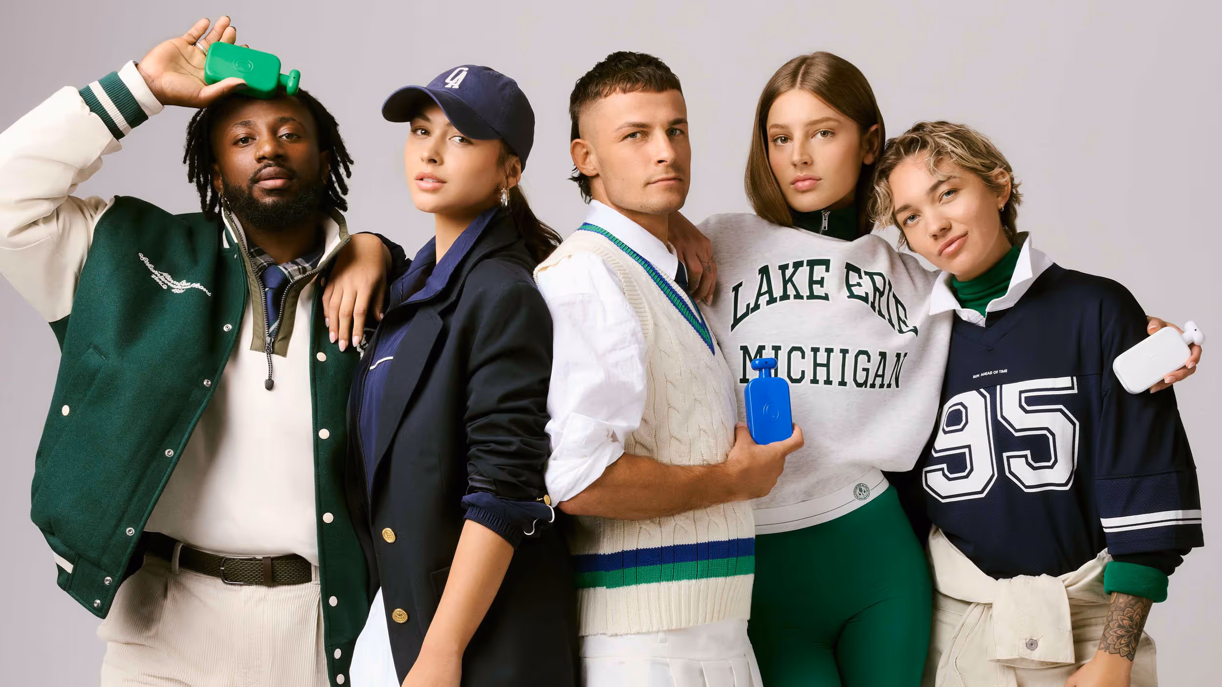 Five diverse young adults standing close together, each holding a colorful hot water bottle and dressed in casual, sporty clothing.
