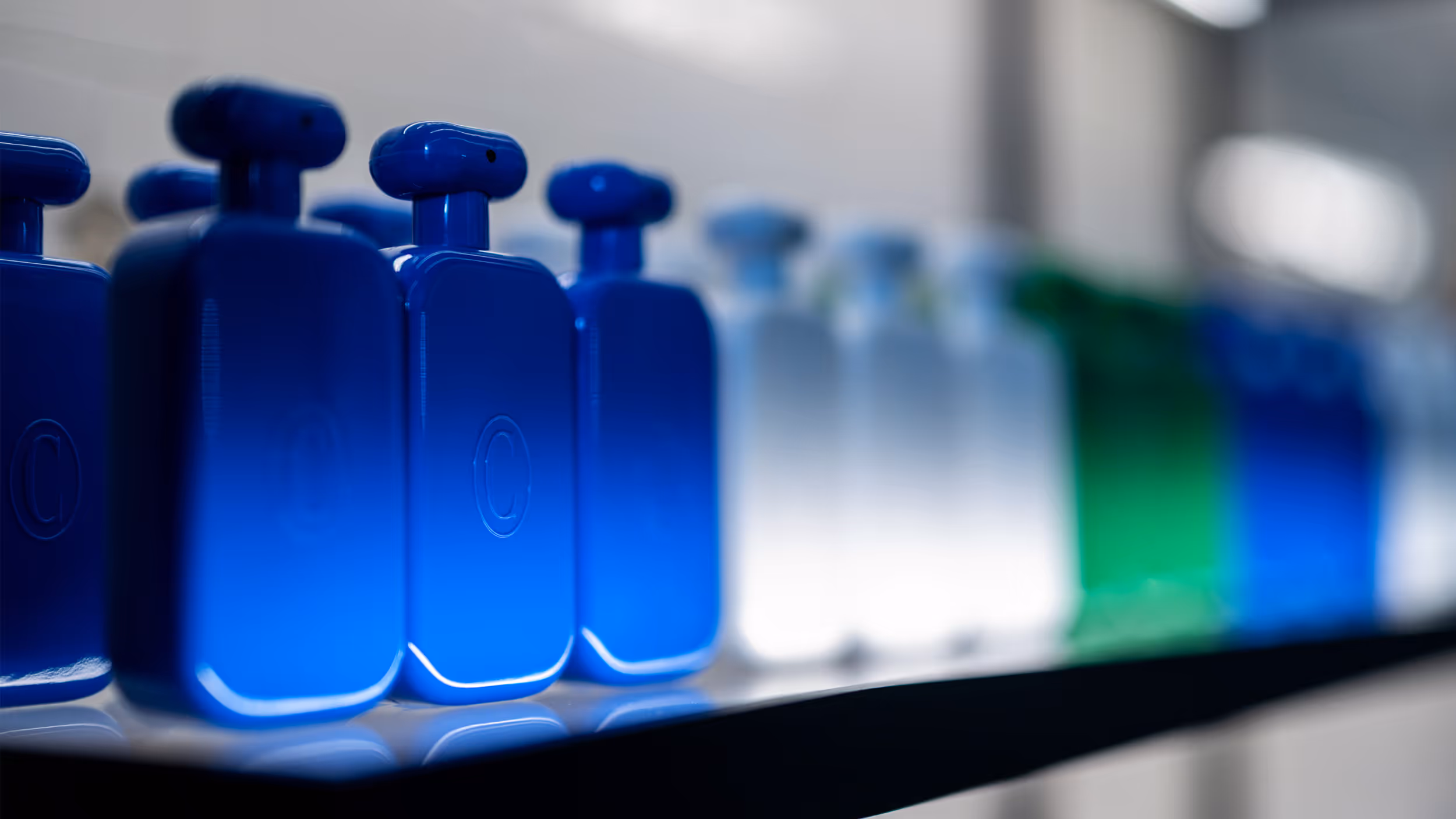 Row of gradient blue, white, and green translucent perfume bottles on a shelf with a blurred background.