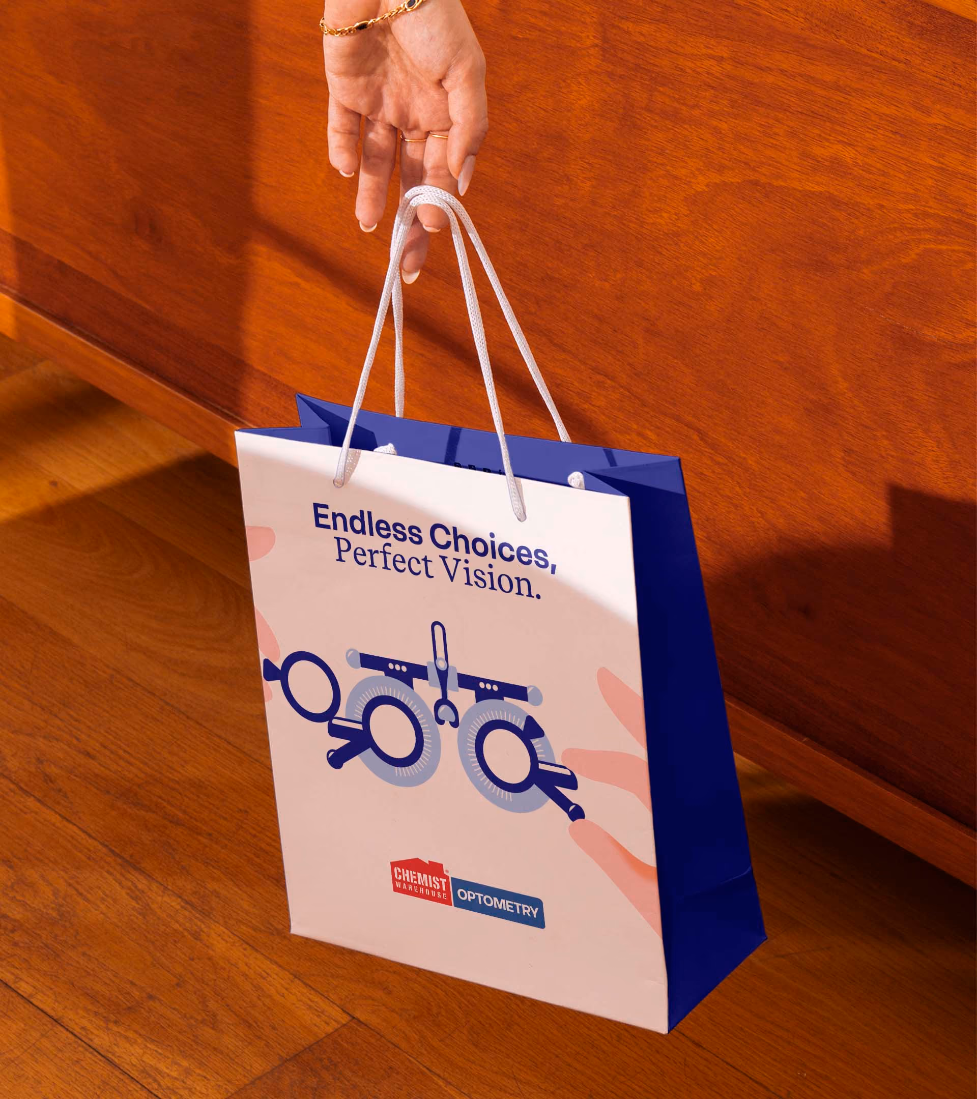 Hand holding a white and blue gift bag with an optometry testing device graphic and text saying 'Endless Choices, Perfect Vision.'