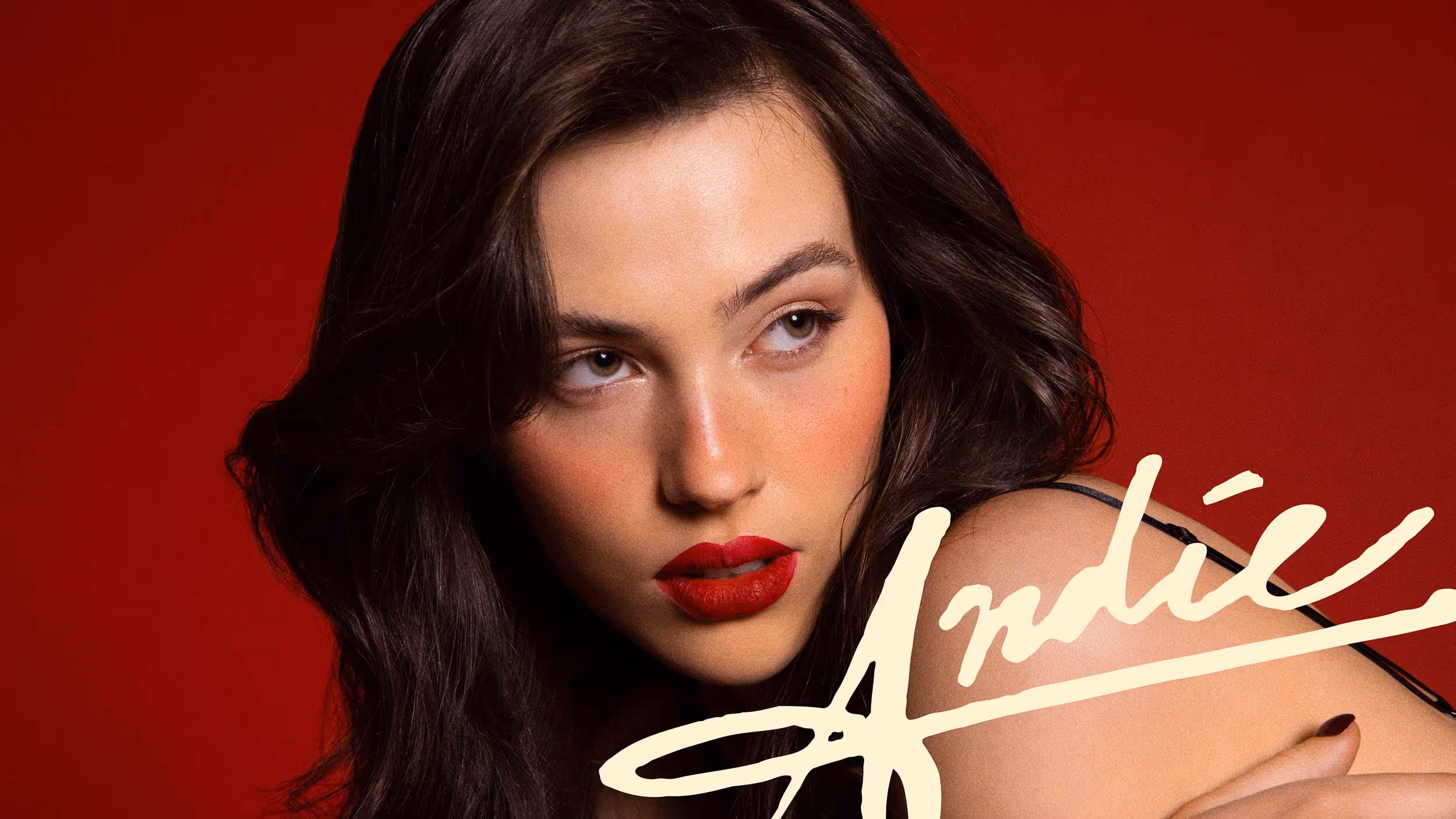 Close-up of a woman with dark hair, red lipstick, and manicured nails against a red background with the word 'Andie' written in cream script.