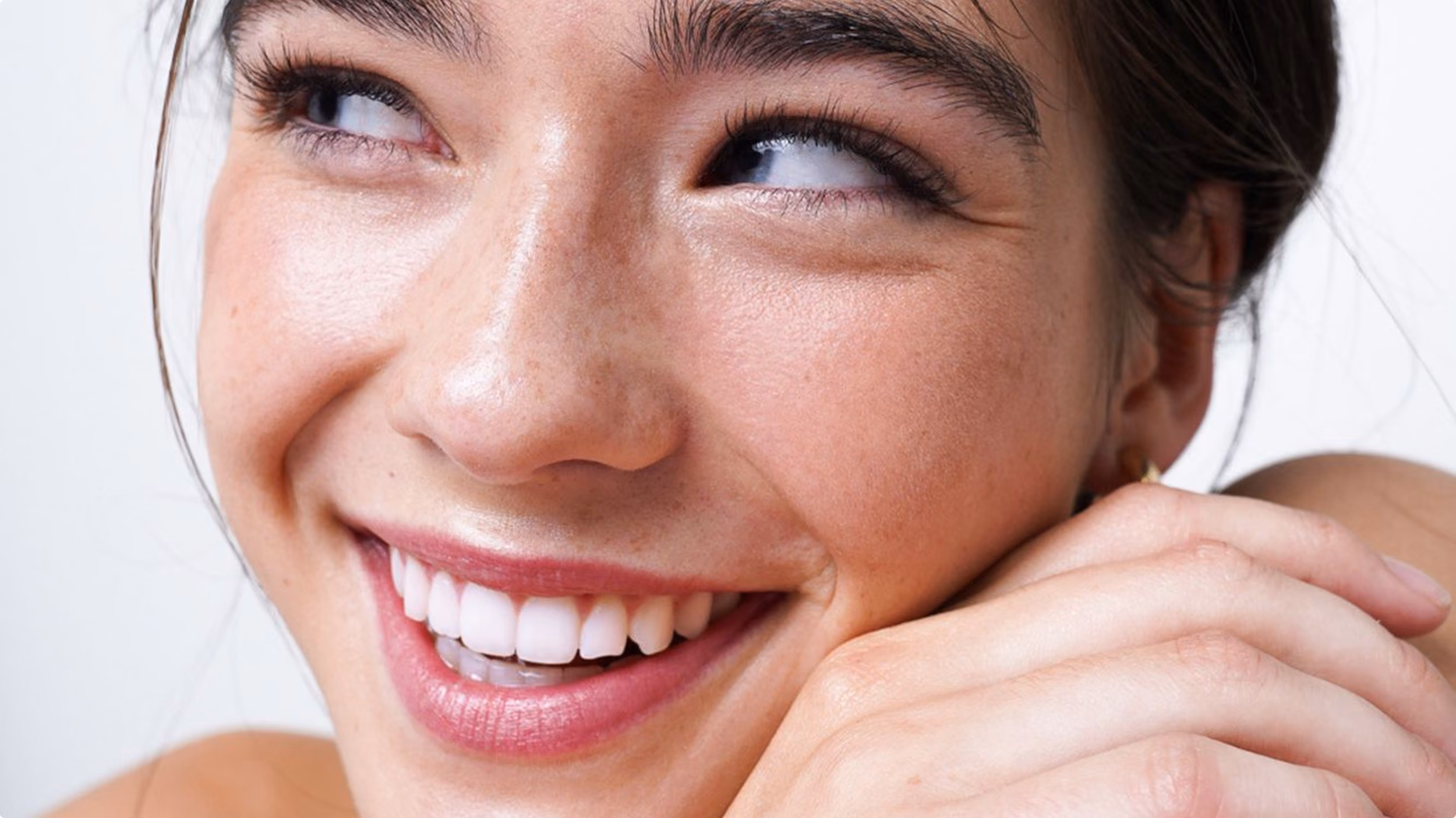Close-up of a smiling woman with clear skin, light freckles, and white teeth looking to the side.