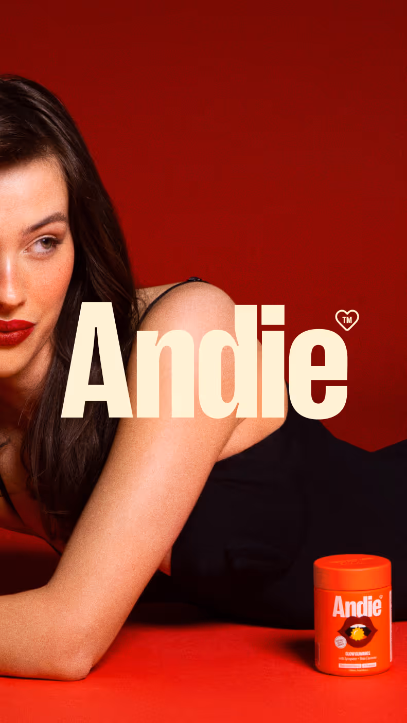 Woman with dark hair and red lipstick lying on red surface with Andie supplement container nearby.