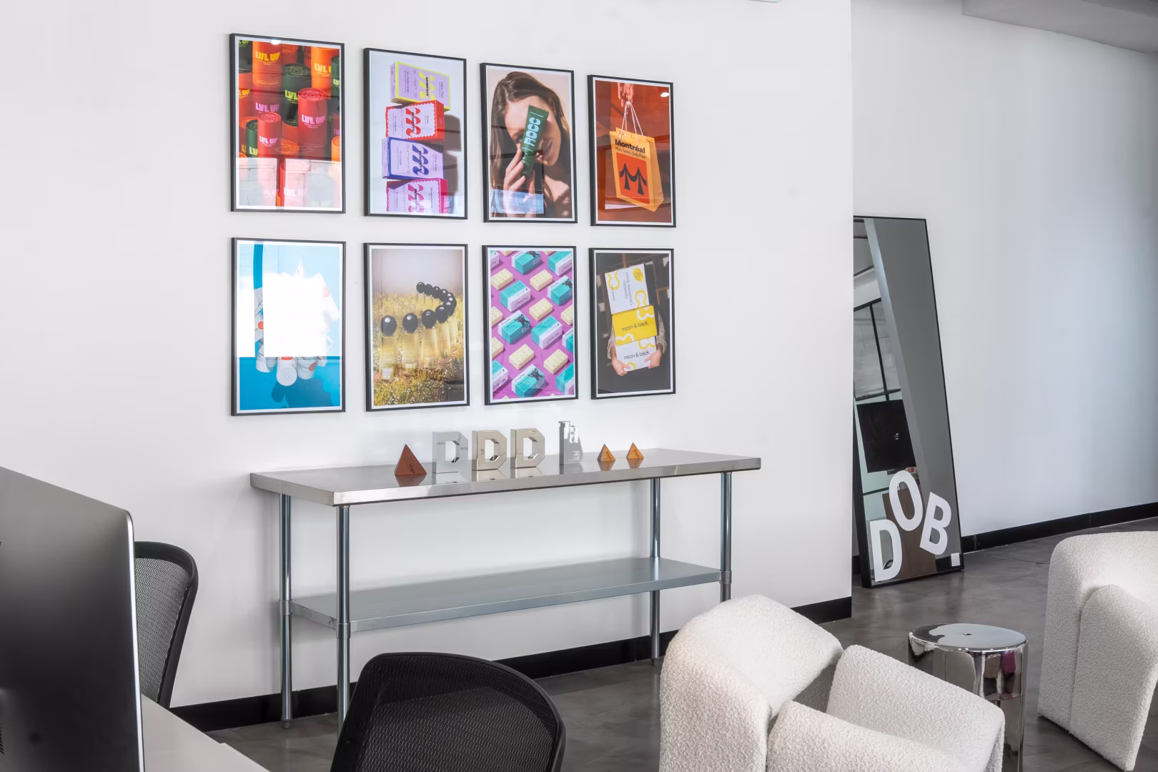 Modern office space with framed art, a metal table with letters P, D, B, and cozy white chairs.