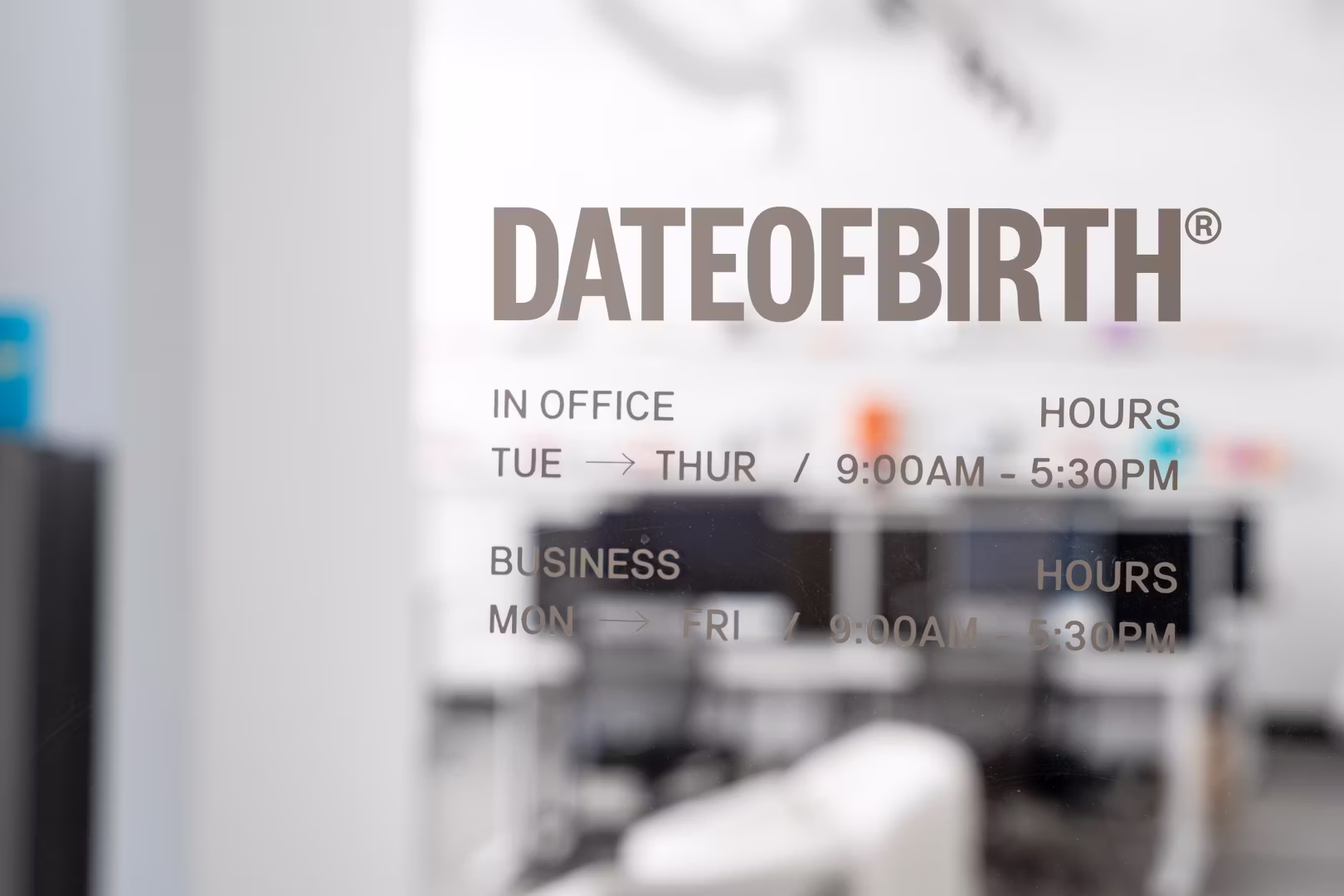Glass door with office hours and business hours text visible through a blurred office interior.