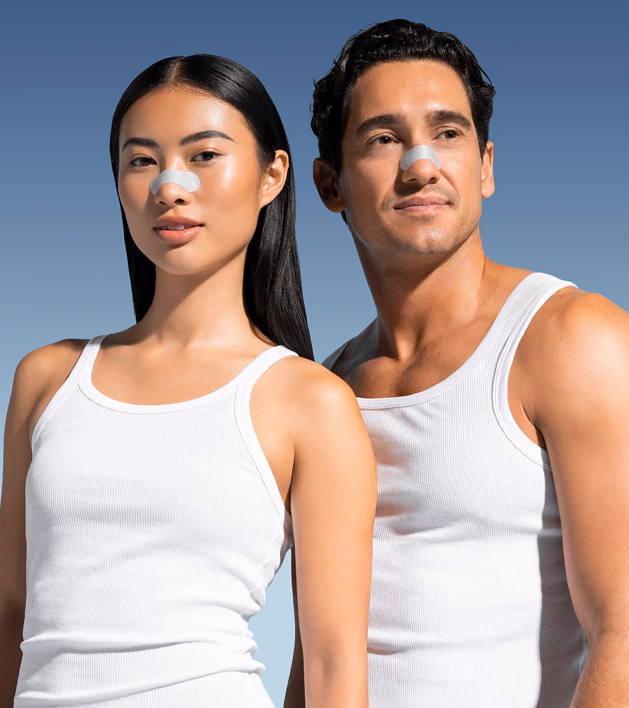A man and woman in white tank tops wear gray nose strips against a blue sky background.