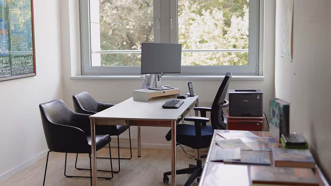 Modernes Büro mit einem Tisch, drei Stühlen, Computerbildschirm vor einem großen Fenster und einem Drucker an der Seite.