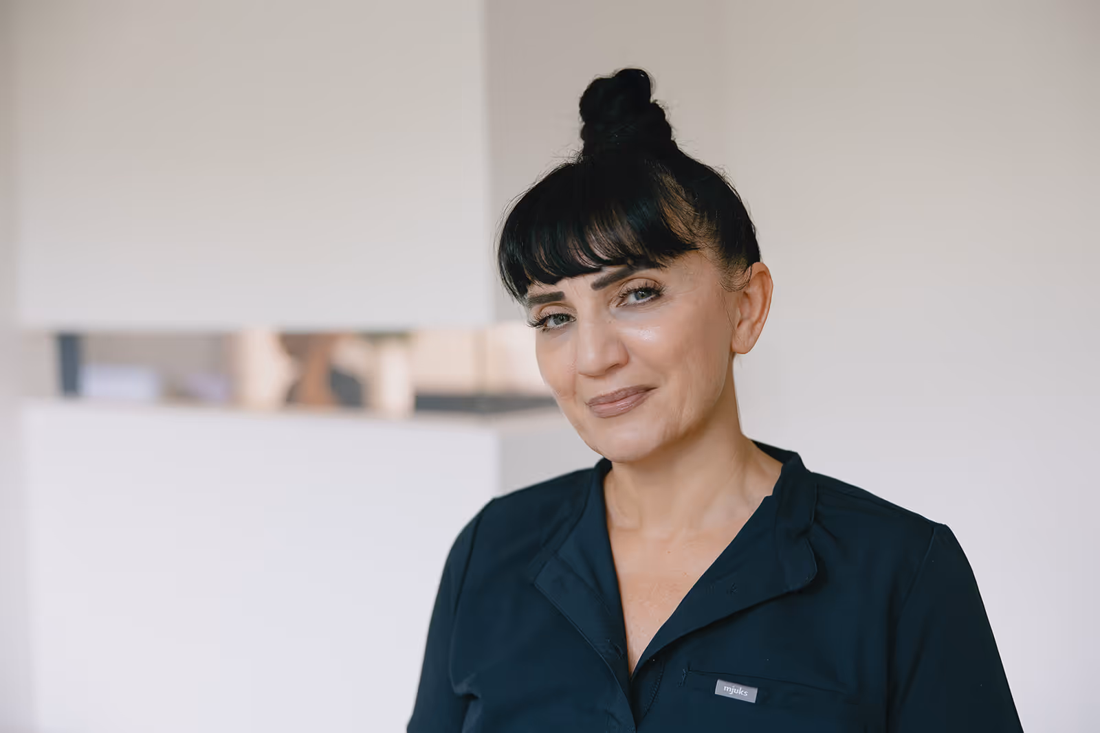 Frau mit dunklen Haaren im Dutt, die ein dunkelblaues Oberteil trägt und in die Kamera lächelt.