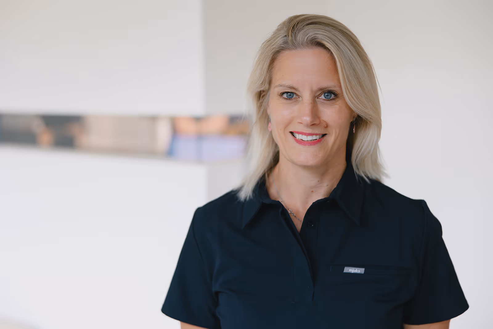 Porträt einer lächelnden blonden Frau in schwarzem Hemd vor weißem Hintergrund.