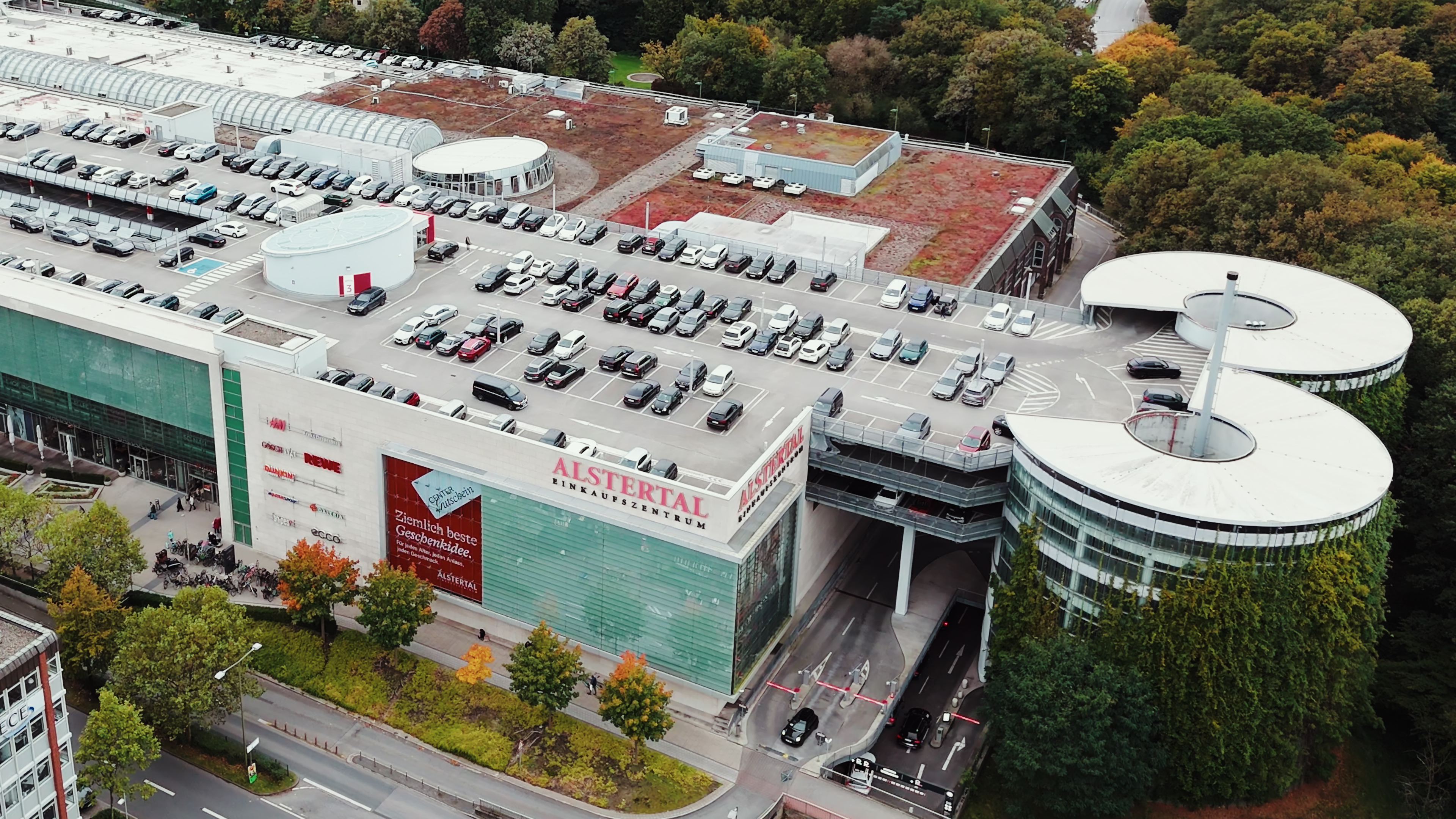Aerial view of Alstertal Einkaufszentrum shopping center with rooftop parking and surrounding trees in autumn.