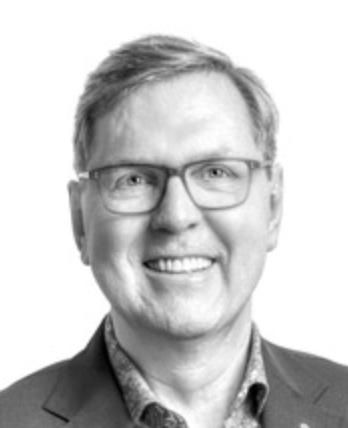 Smiling middle-aged man with glasses, wearing a suit jacket and patterned shirt against a white background.