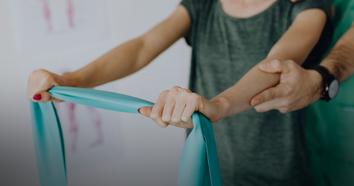 Eine Person dehnt ein hellblaues Widerstandsband, während eine andere Person ihren Arm zur Unterstützung hält.