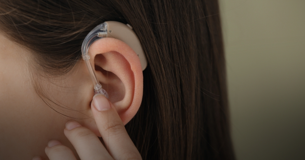 Nahaufnahme eines Ohrs mit einem Hörgerät, das von einer Person mit braunen Haaren getragen wird.