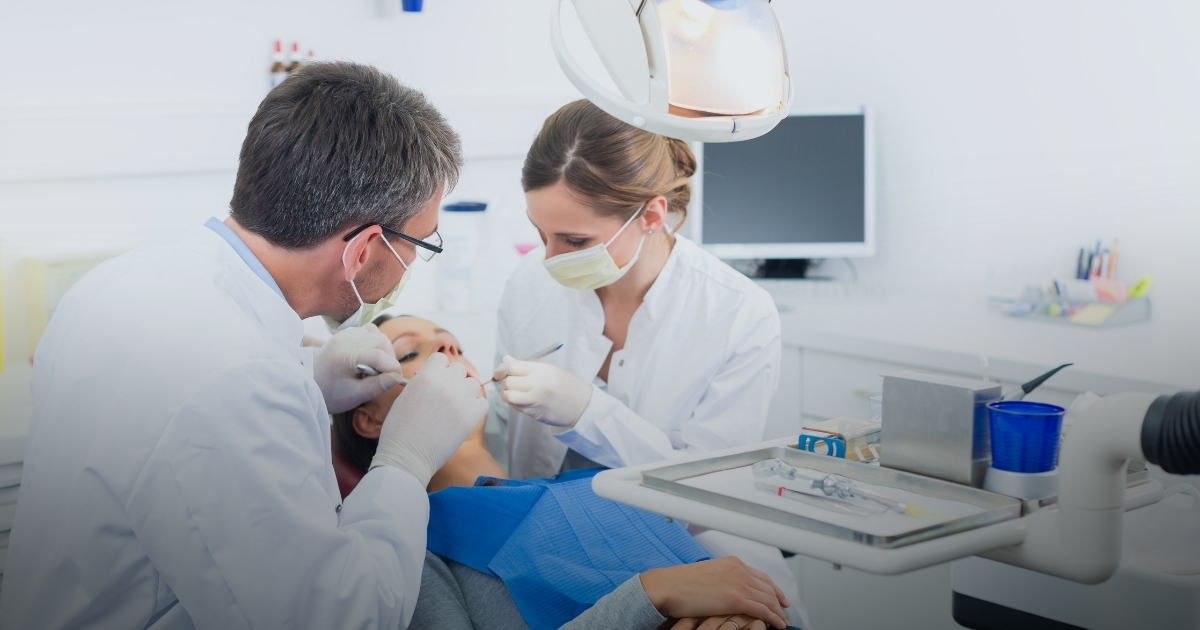 Zahnarzt und Assistentin behandeln Patientin im Zahnarztstuhl in einer modernen Praxis.