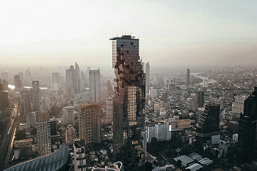 Cityscape with a tall modern skyscraper featuring a pixelated facade among other high-rise buildings at sunset.
