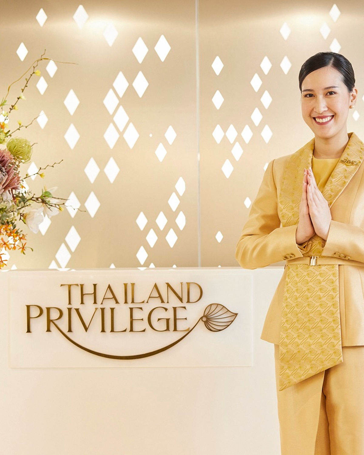 Woman in traditional golden Thai attire performing a respectful wai gesture next to a Thailand Privilege sign.