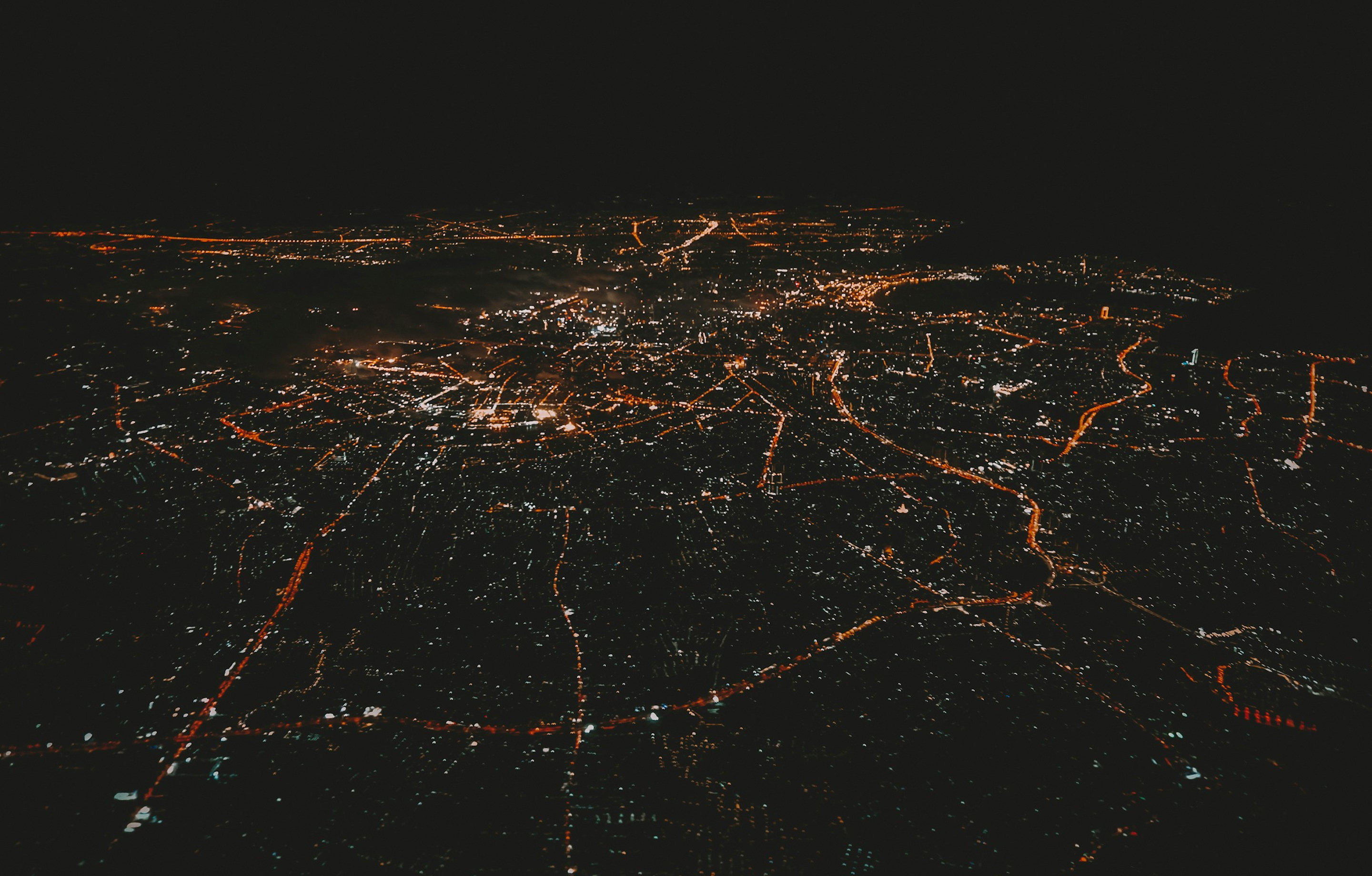 Aerial night view of a sprawling city illuminated by orange streetlights and white building lights.
