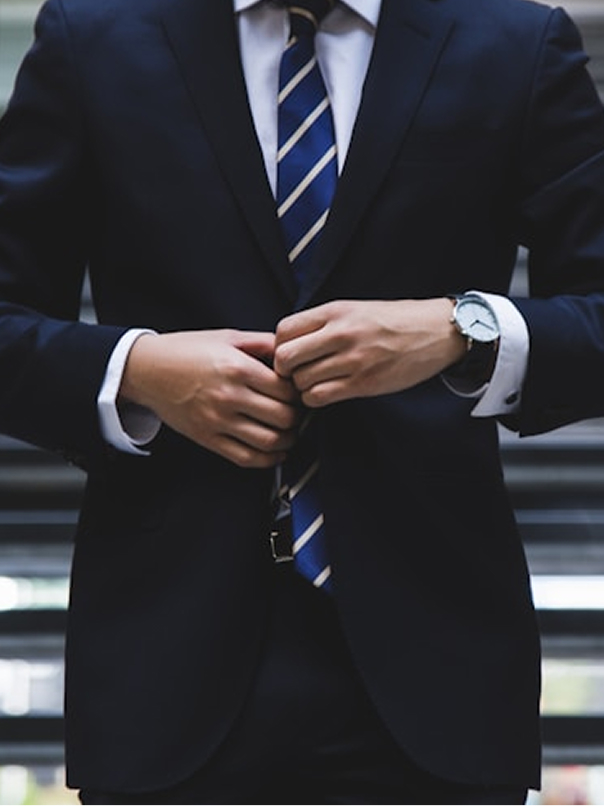 Man adjusting his navy blue suit jacket and striped tie, wearing a watch on his left wrist.