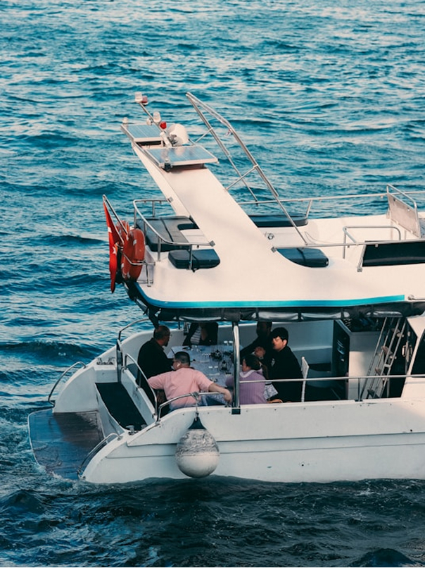 People sitting and dining on the rear deck of a white boat floating on blue water.