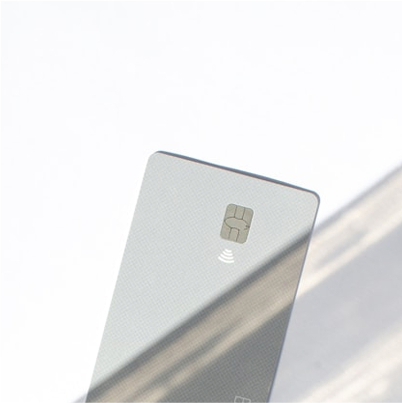 Close-up of a silver credit card with a chip and contactless payment symbol against a bright background.