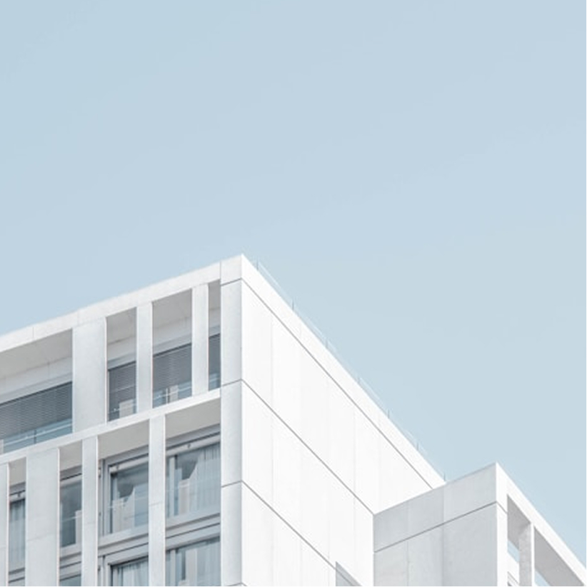 Upper corner of a modern white building with large vertical windows against a clear blue sky.
