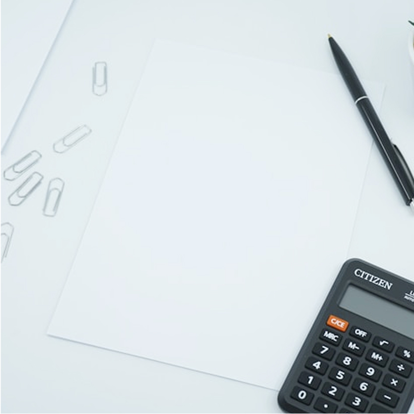 Blank white paper on a white desk surrounded by paper clips, a black pen, and a calculator.