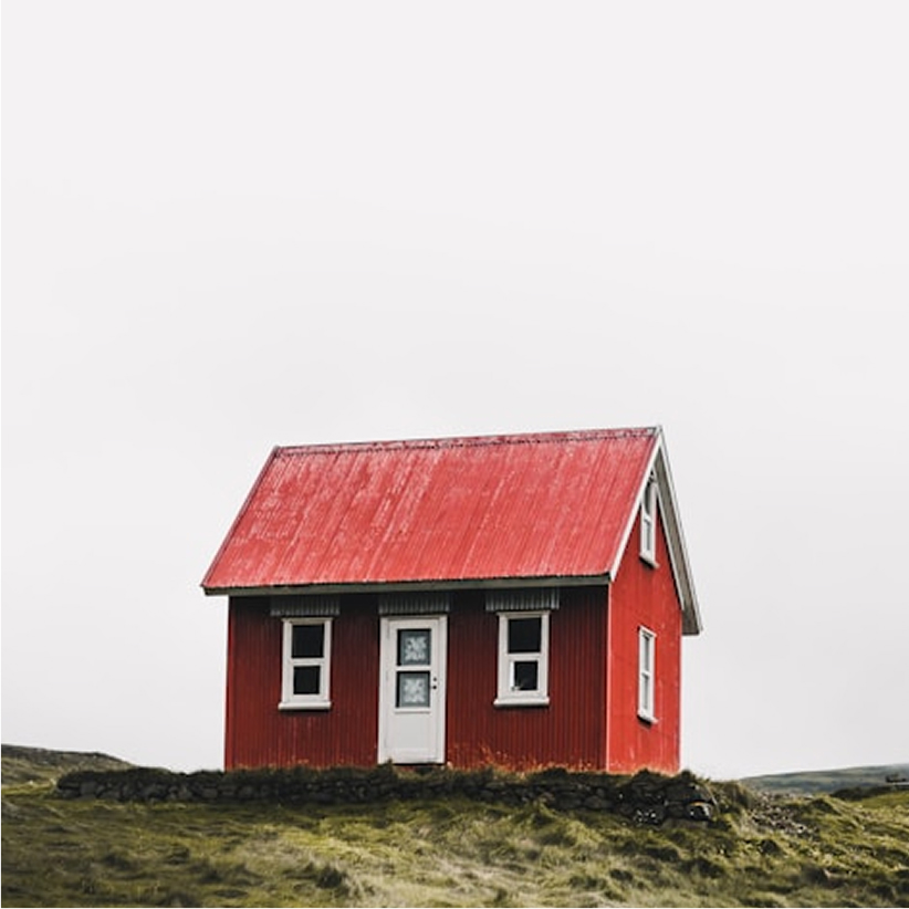 Small red wooden house with a red roof on grassy terrain under an overcast sky.