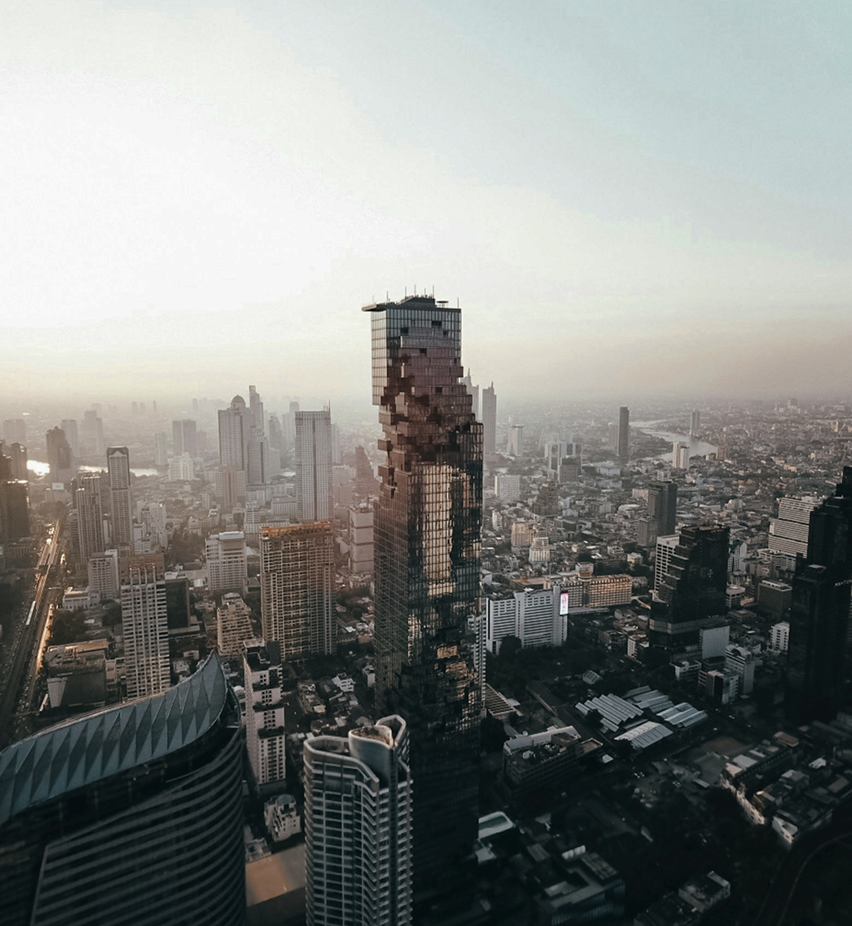 Aerial view of a cityscape featuring the pixelated design of the MahaNakhon skyscraper at sunset.