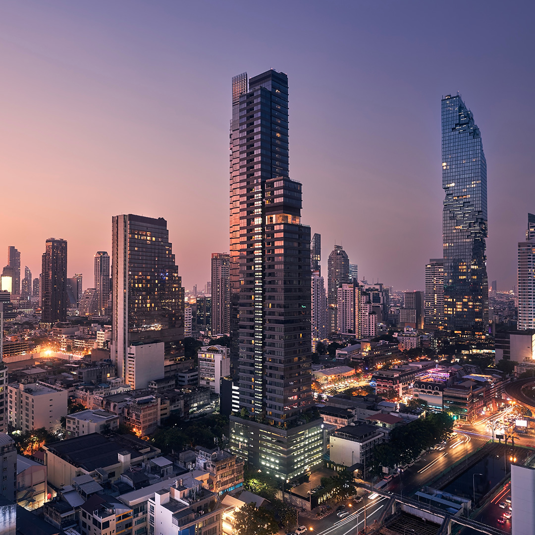 City skyline at dusk with illuminated modern skyscrapers and busy streets below.