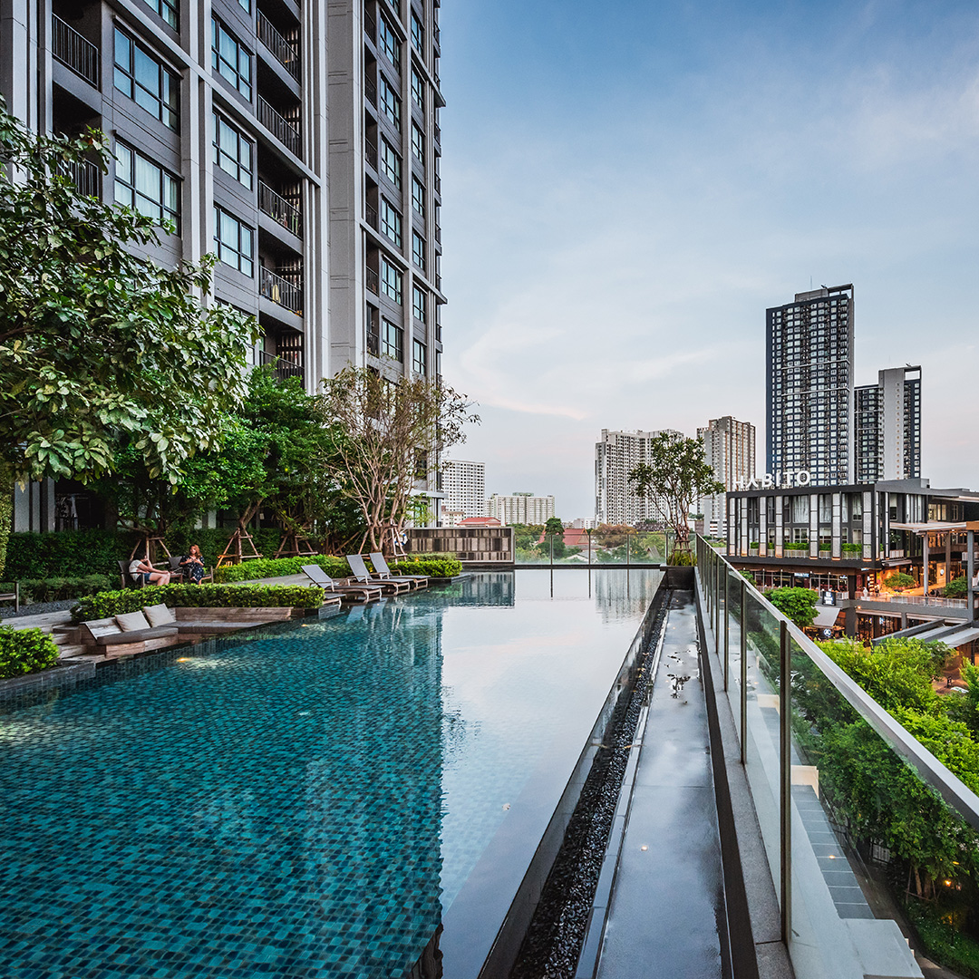Modern outdoor swimming pool with lounge chairs beside a high-rise building overlooking a city skyline at dusk.