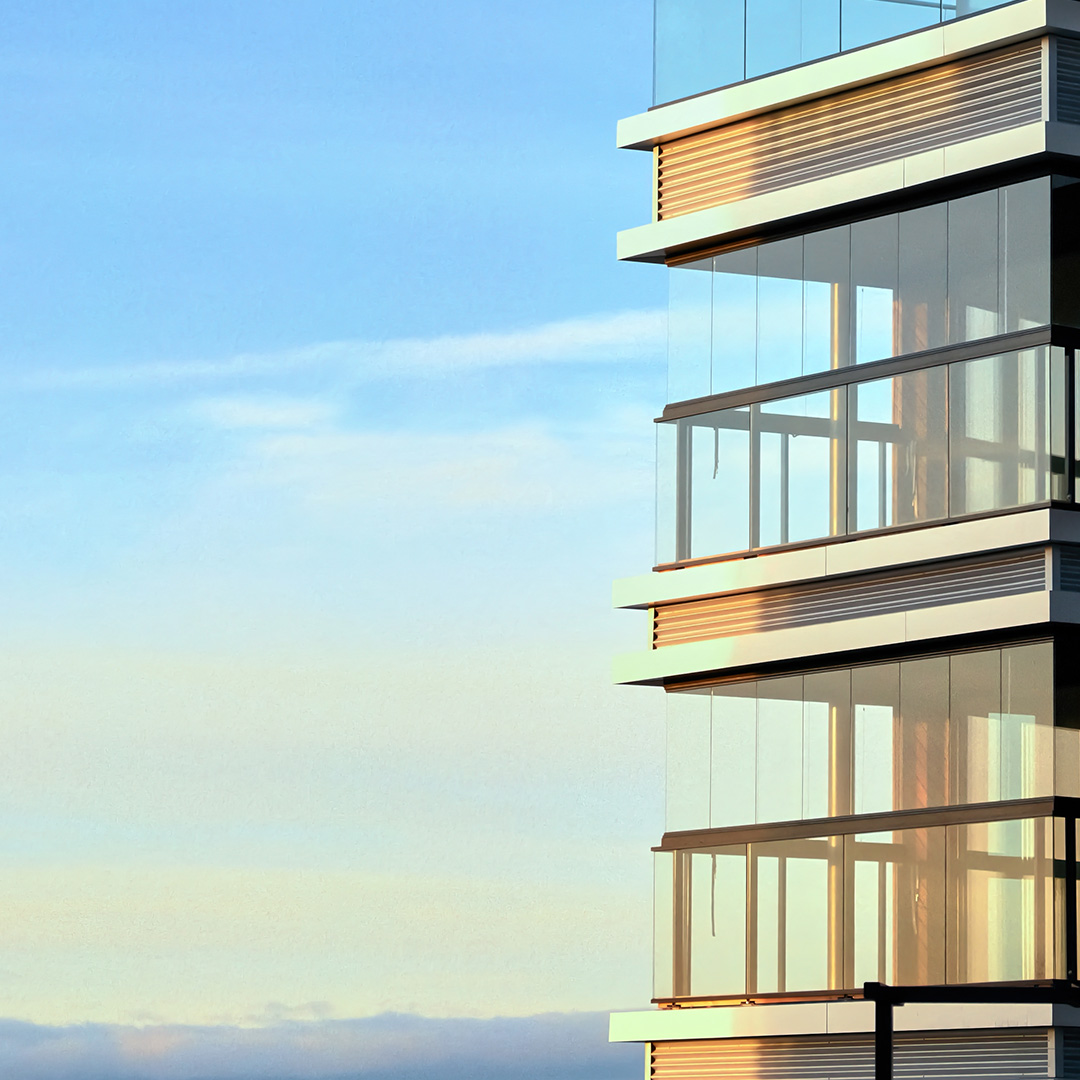 Close-up of modern glass balconies on a building at sunset with a clear blue sky background.