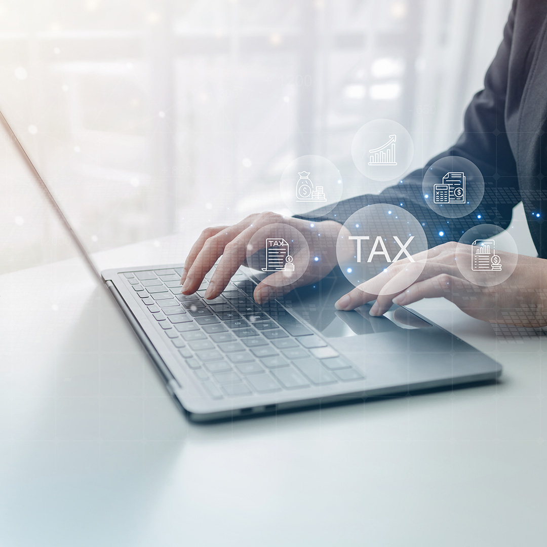 Hands typing on a laptop keyboard with floating financial icons and the word 'TAX' overlayed.