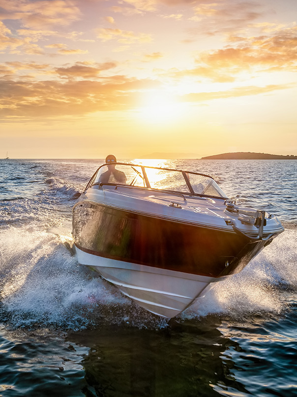 Speedboat cutting through water at sunset with a person steering and an island on the horizon.