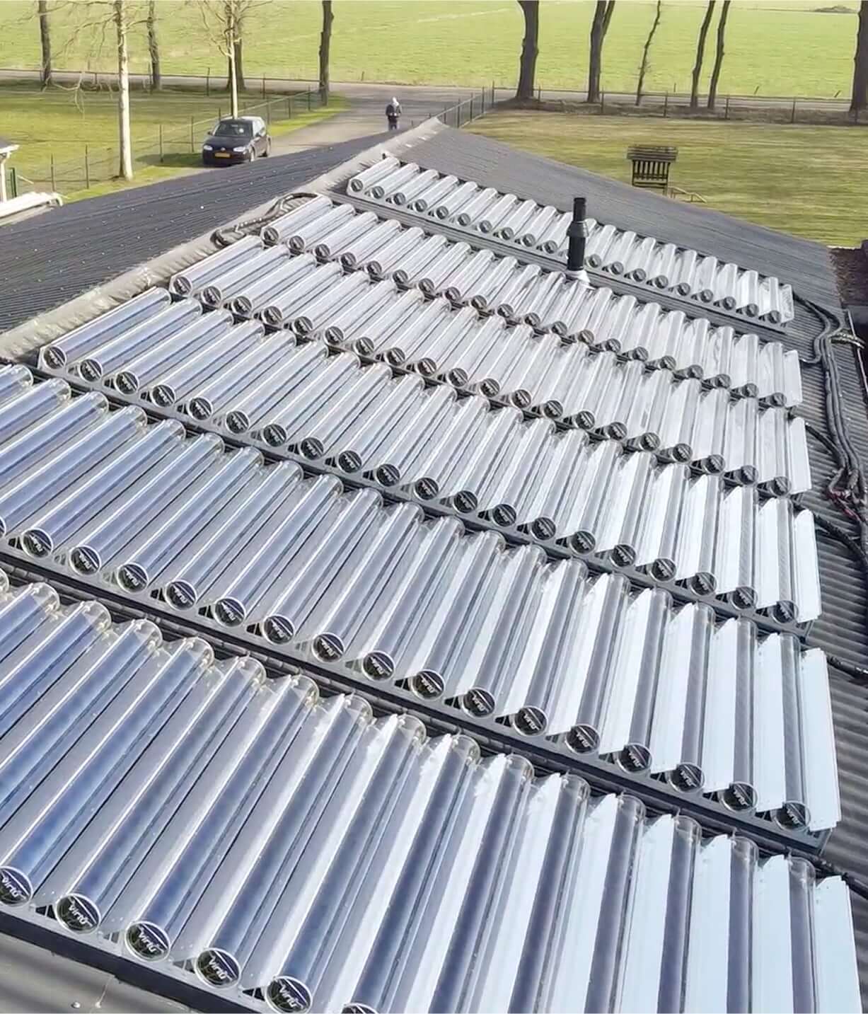 Solar thermal collector tubes installed on a rooftop with a grassy background and a person walking on a path.