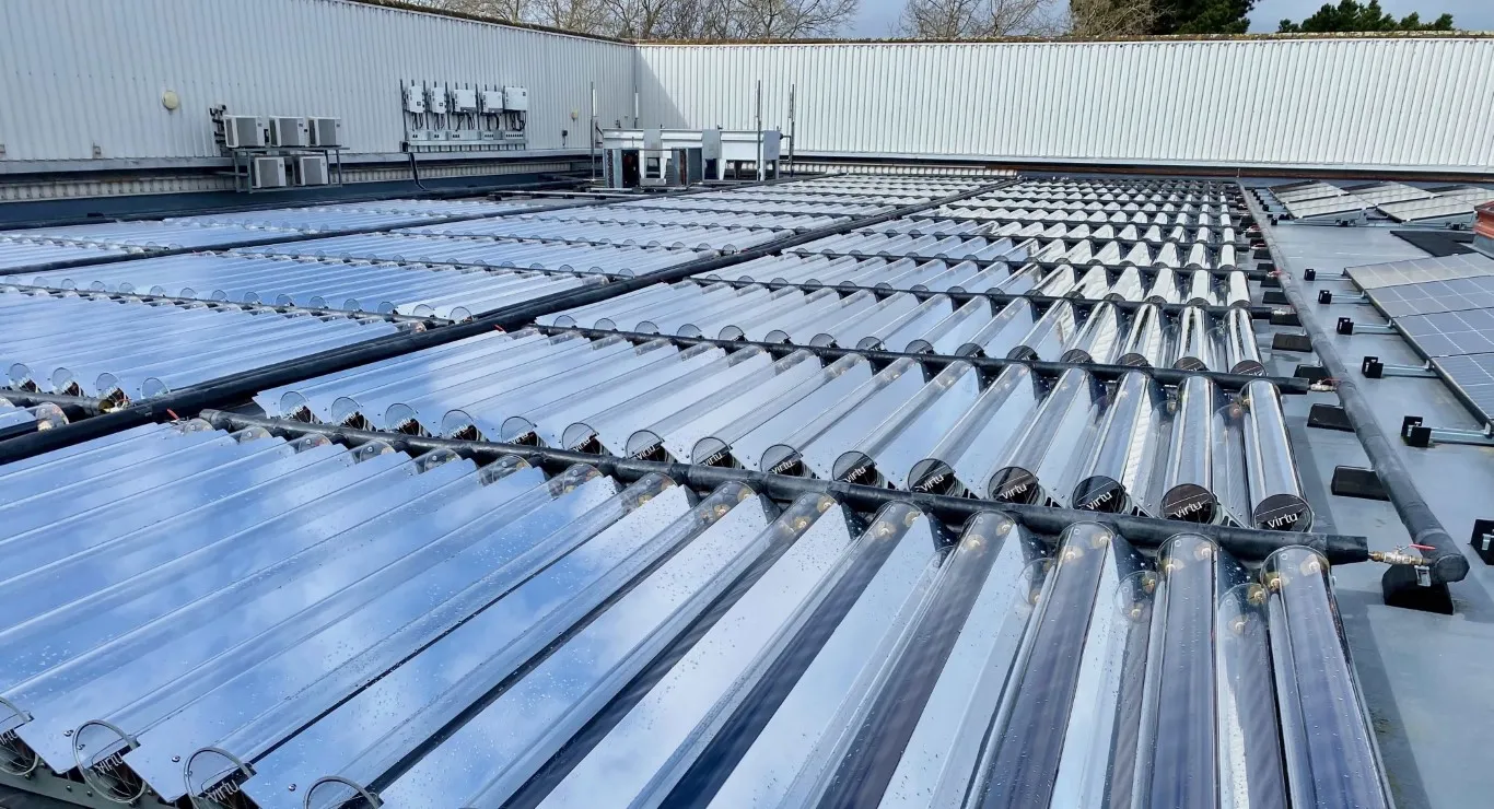 Rooftop solar thermal panels with rows of glass vacuum tubes and some solar panels on the right side.