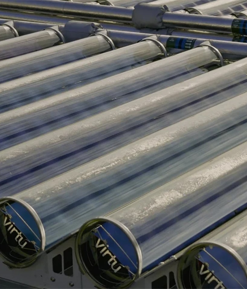 Close-up of multiple parallel glass vacuum tubes of solar thermal collectors with a reflection of the sky.