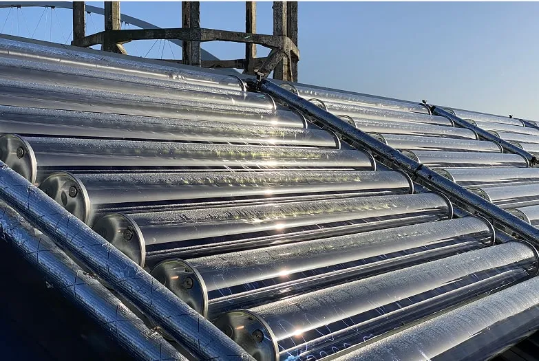 Rows of shiny metallic solar thermal tubes reflecting sunlight with a clear blue sky in the background.