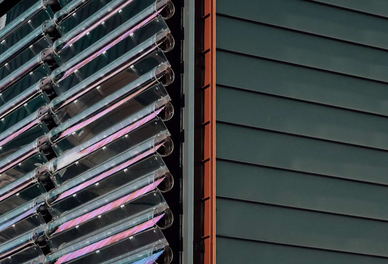 Close-up of angled transparent solar tubes attached to a building's facade next to vertical metal siding.