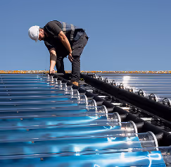 Worker in a white helmet inspecting solar panels installed on a roof under clear blue sky.