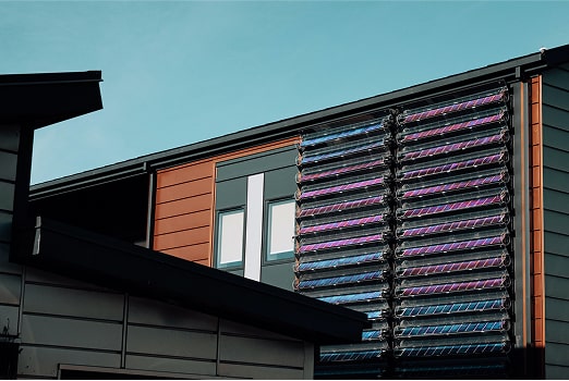 Modern building facade with colorful solar panel arrays mounted vertically on the exterior wall under a clear blue sky.