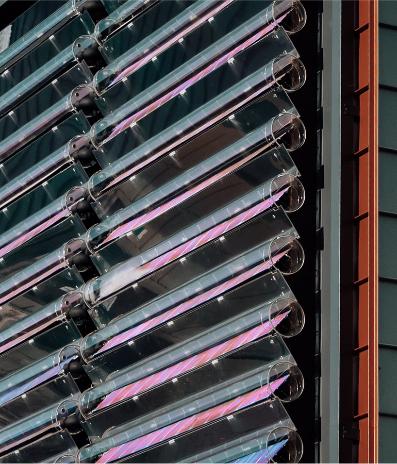 Close-up of angled cylindrical glass tubes with pink reflections on a modern building facade.