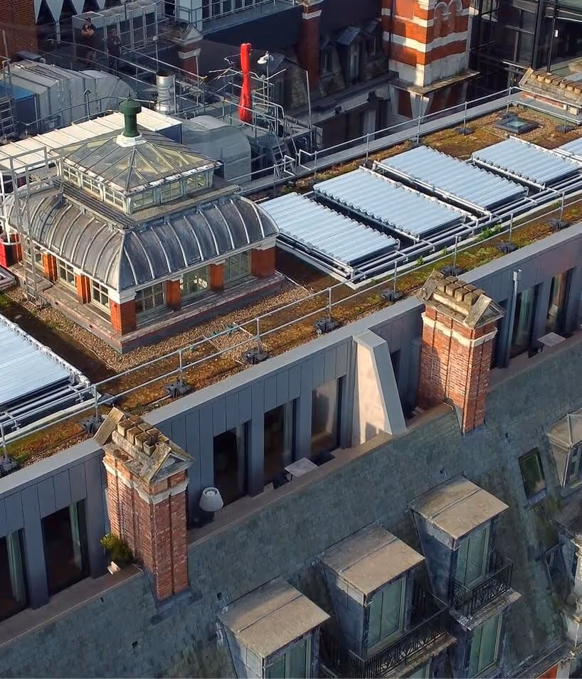 A rooftop with skylights, solar thermal panels, and a glass-domed structure surrounded by brick chimneys and modern grey siding.