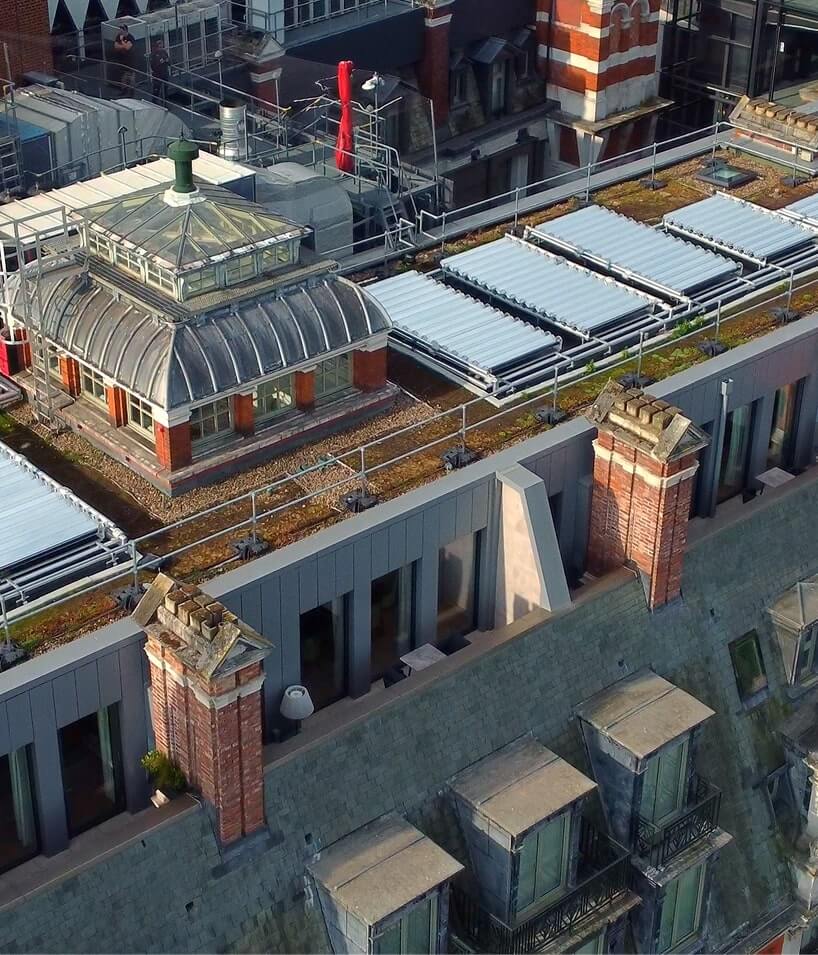 A rooftop with skylights, solar panels, and a glass-domed structure surrounded by brick chimneys and modern grey siding.