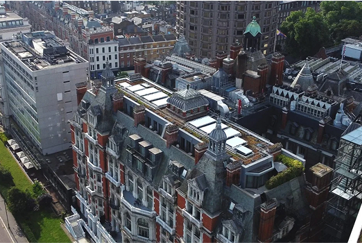 Aerial view of a historical multi-story building with detailed brick and stone architecture surrounded by other buildings and greenery.