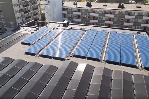 Paneles solares instalados en la azotea de un edificio urbano con otros edificios residenciales al fondo.