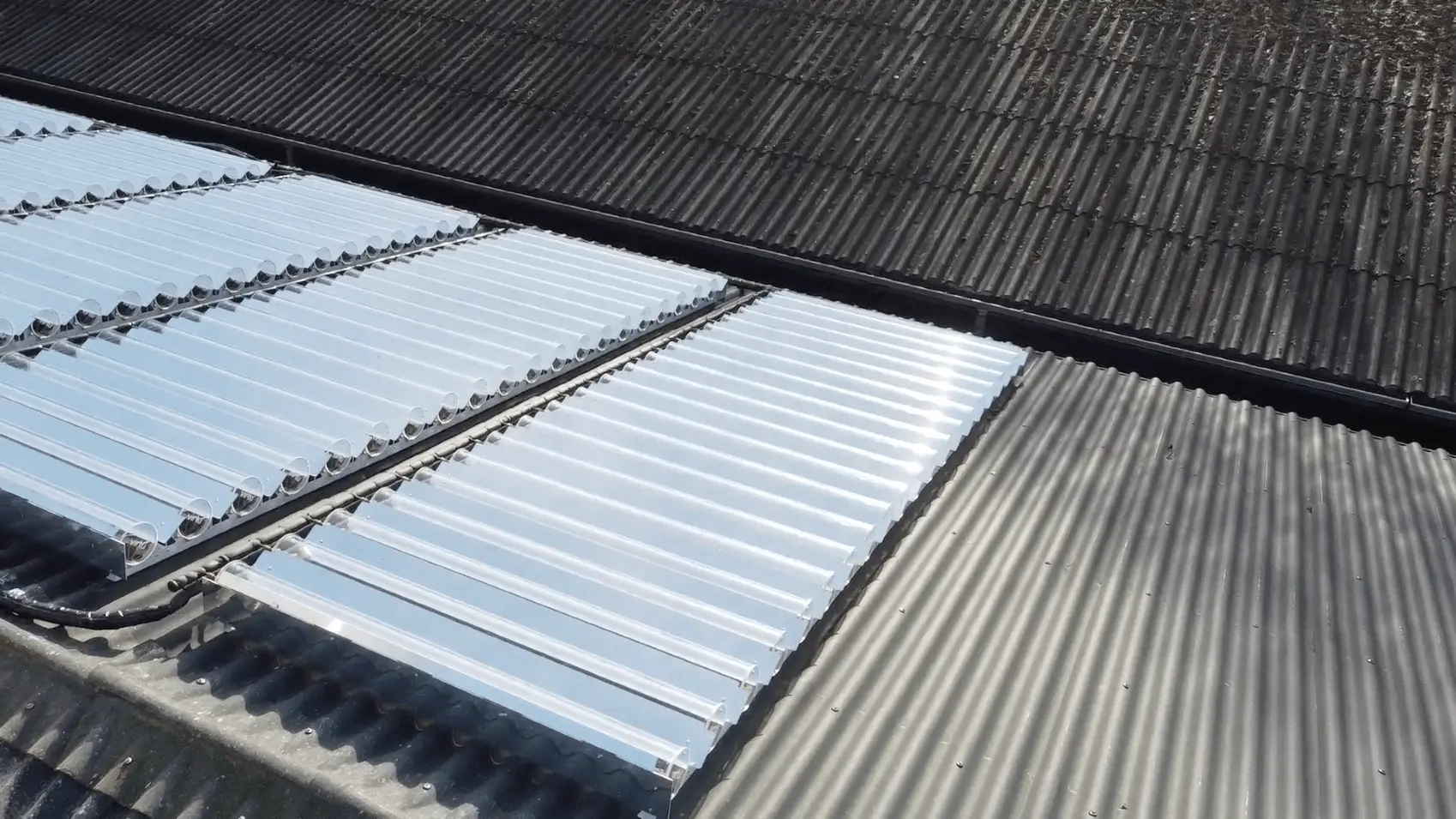 Corrugated rooftop panels with transparent solar thermal tubes installed on some sections.