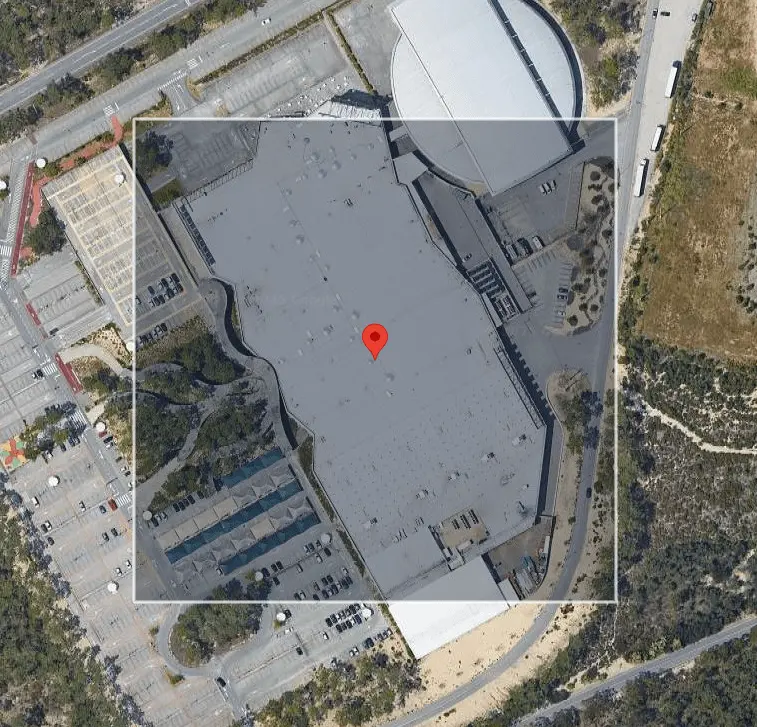 Aerial view of a large building with surrounding parking lots and roads, marked by a red location pin at the center.