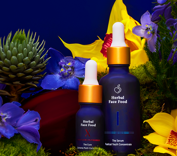 Two dark blue dropper bottles labeled Herbal Face Food surrounded by colorful flowers and greenery.